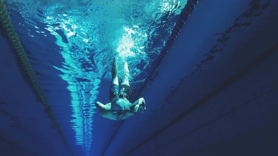 Athlete in swimming gear checking goggles fit before entering water for workout session