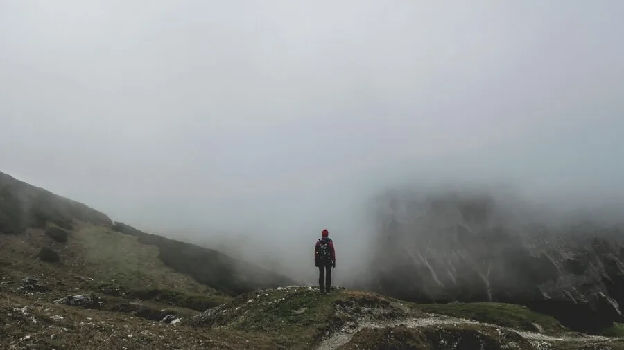 Backpacker hiking through misty mountain terrain with rain clouds overhead