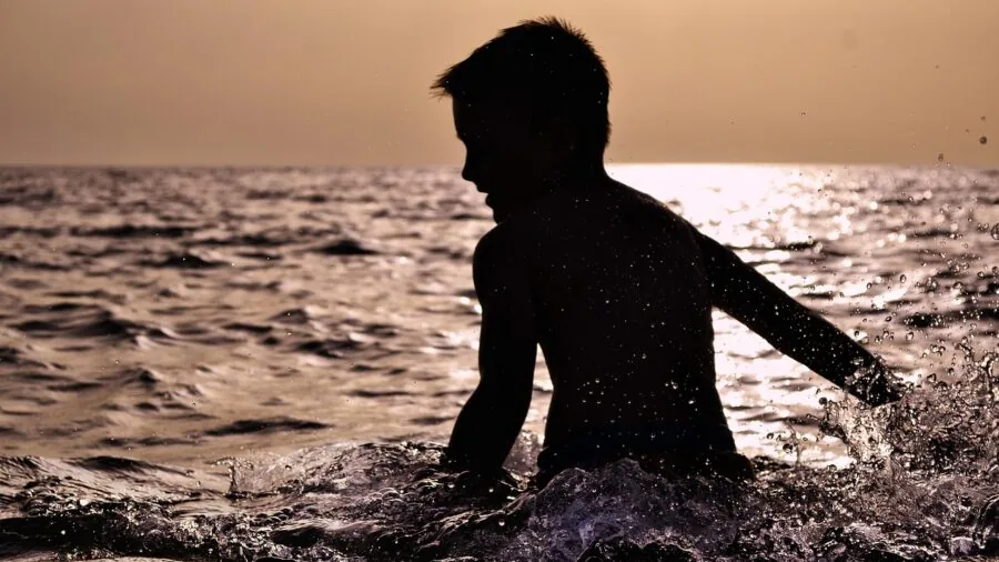 Child playing outdoors getting wet with water splash, demonstrating active play and durability needs
