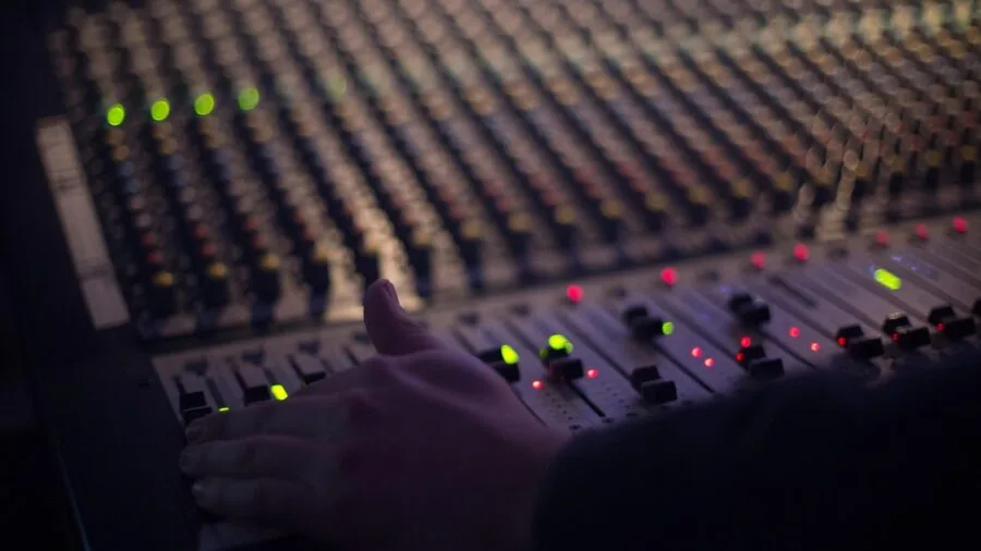 Close-up of hands reaching for audio equipment controls during live streaming session