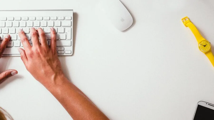 Close-up of hands typing on a mechanical keyboard at a wooden desk with warm lighting