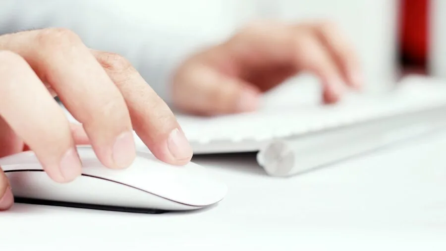 Close-up of person's hand using a mouse while working at a wooden desk with laptop