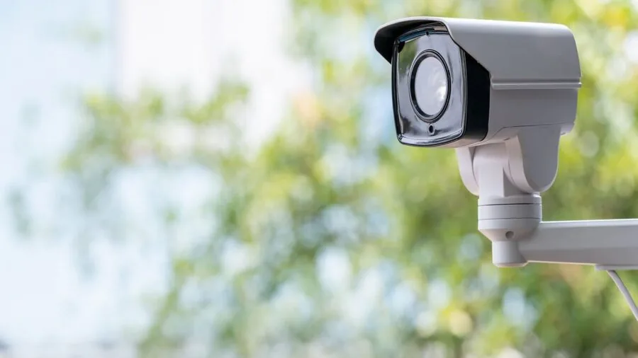Homeowner installing wired security camera on exterior wall of house