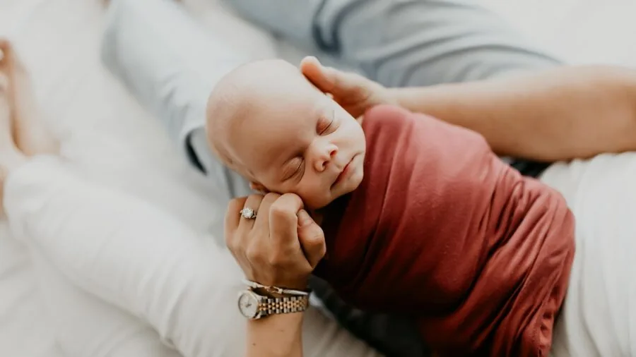 Parent quietly watching sleeping baby in nursery from doorway at night