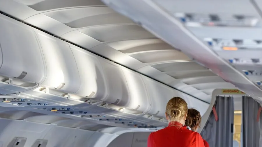 Passenger sitting by airplane window during flight with natural cabin lighting and clouds visible outside