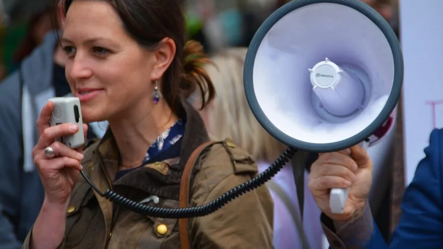 Person carrying compact speaker on hiking trail in natural landscape
