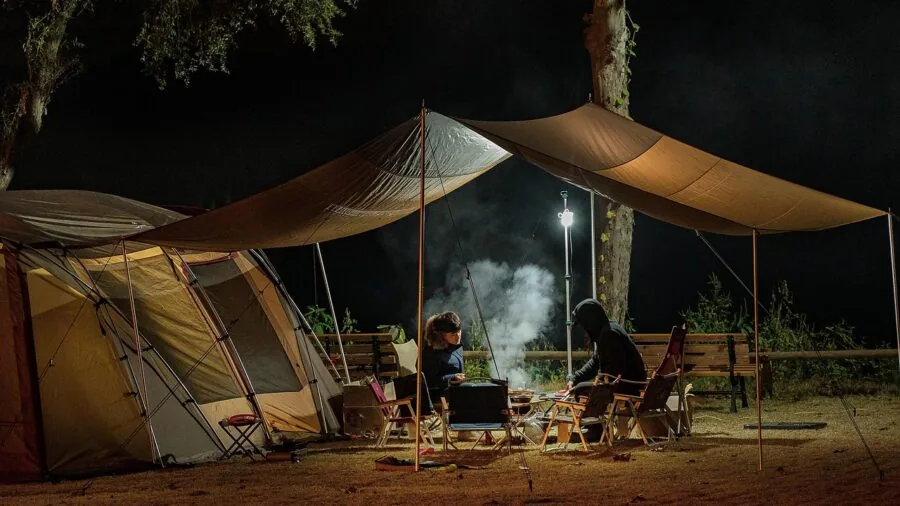 Person charging devices at campsite with tent and natural landscape in background