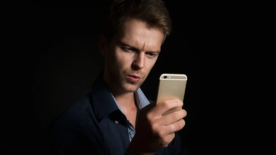 Person checking smartphone in busy city street with buildings and wireless signals