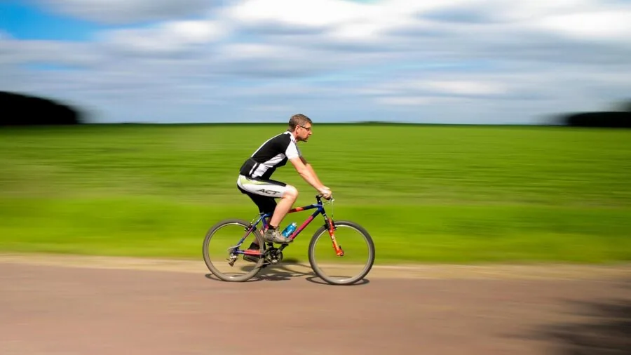 Person cycling on outdoor path while wearing open-ear headphones, demonstrating real-world usage during active commute