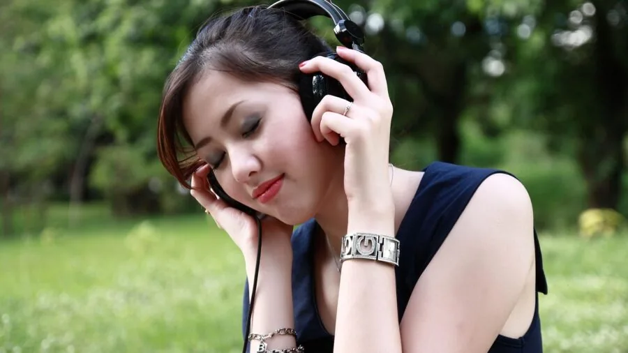 Person enjoying music outdoors in natural setting, wearing wireless earbuds while relaxed in nature