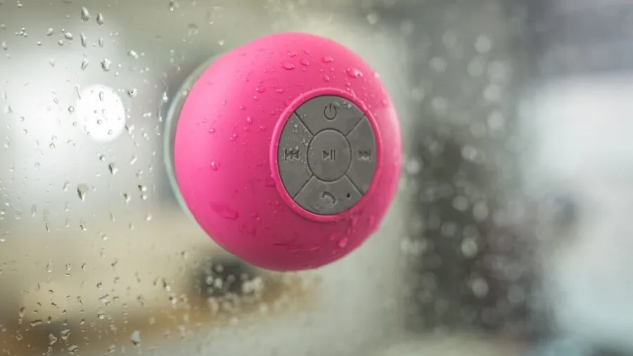 Person enjoying portable speaker by water during outdoor activity, demonstrating durability and water resistance