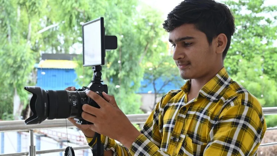 Person filming outdoors with camera on shoulder, natural lighting, focused on video recording