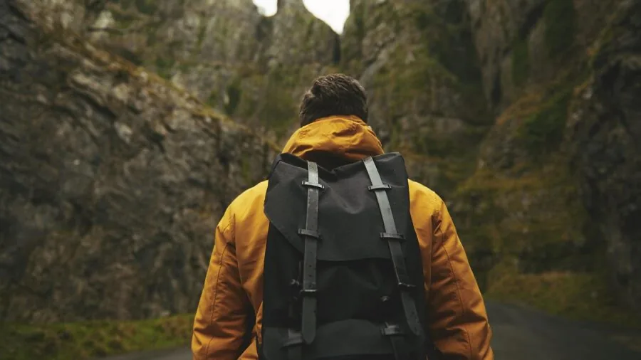 Person hiking on mountain trail with backpack and outdoor gear in natural landscape