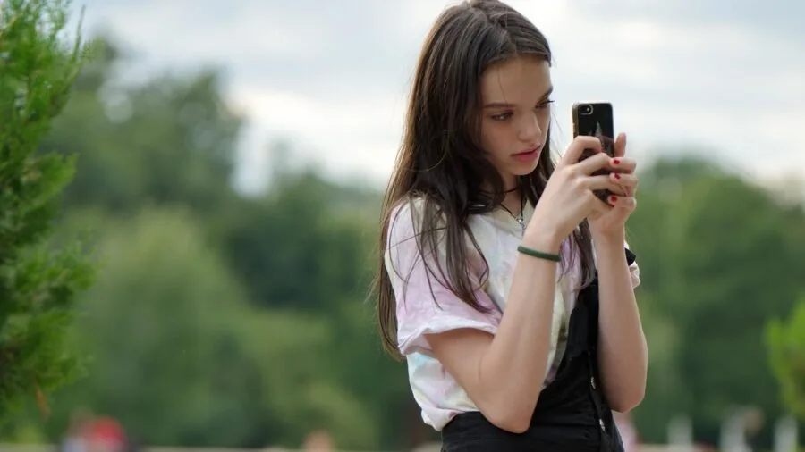 Person holding a smartphone while standing outdoors, demonstrating everyday durability and portability of modern devices
