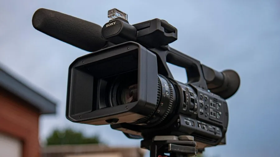 Person holding compact camera recording video in natural outdoor setting with scenic background