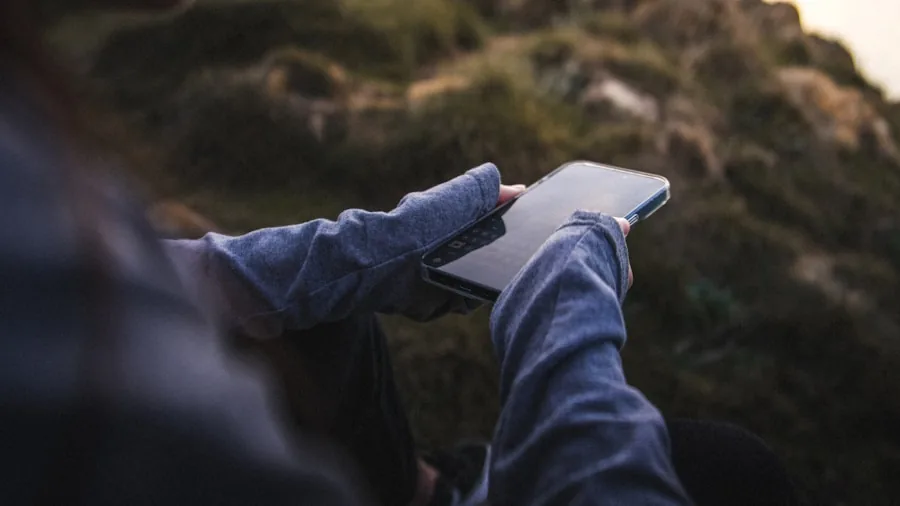 Person holding smartphone while walking outdoors with wireless earbuds in use, demonstrating mobile connectivity