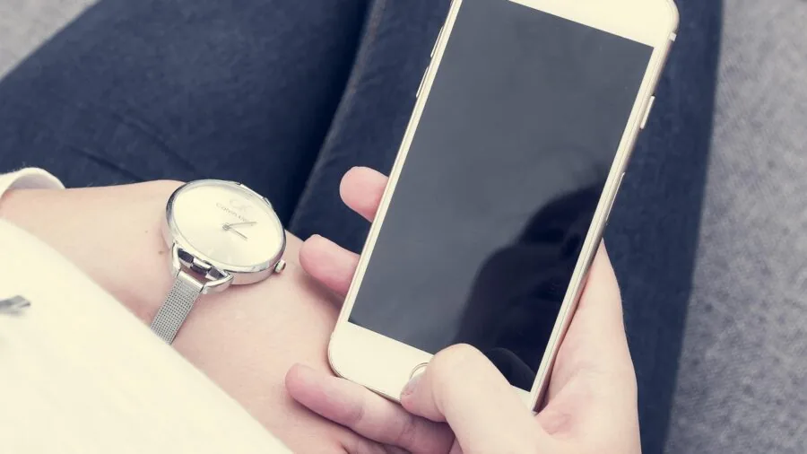 Person holding smartphone with wireless earbuds, representing connected device ecosystem and smart technology integration
