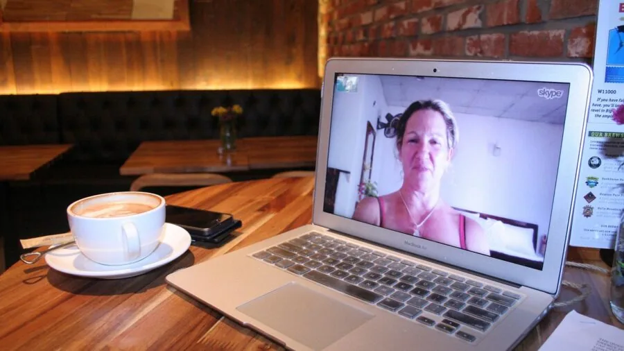 Person in home office during video call with laptop, showing real-world video conferencing environment