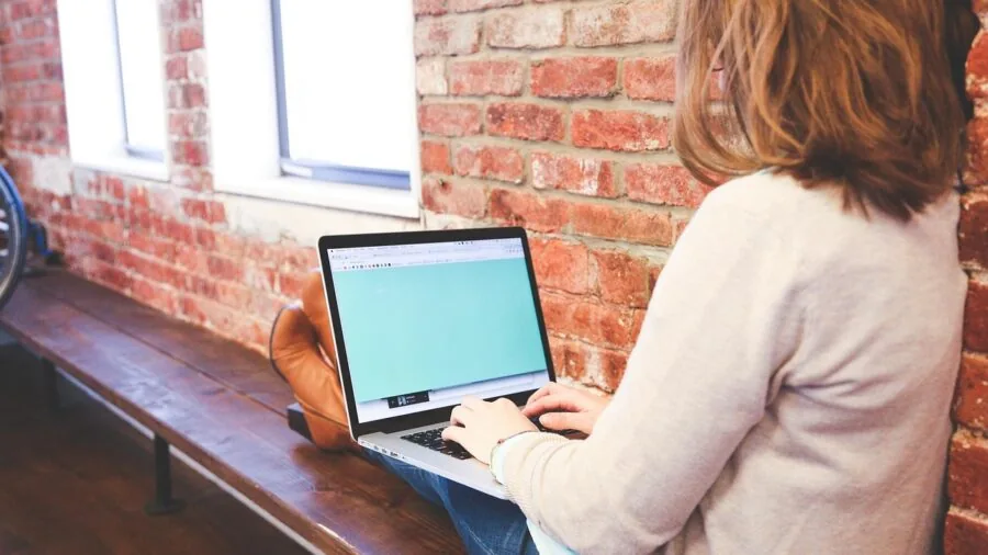 Person multitasking with laptop and notes while working on projects at desk