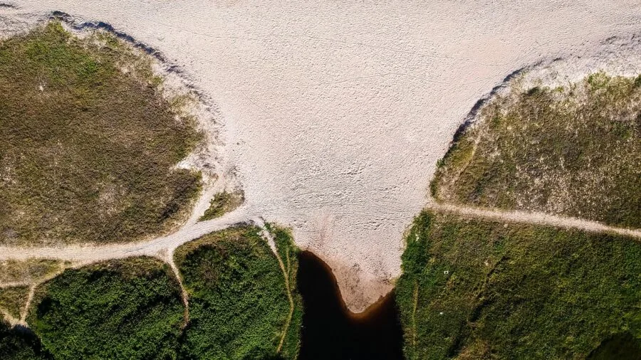 Person operating drone controller while flying over scenic landscape with clear sky visibility