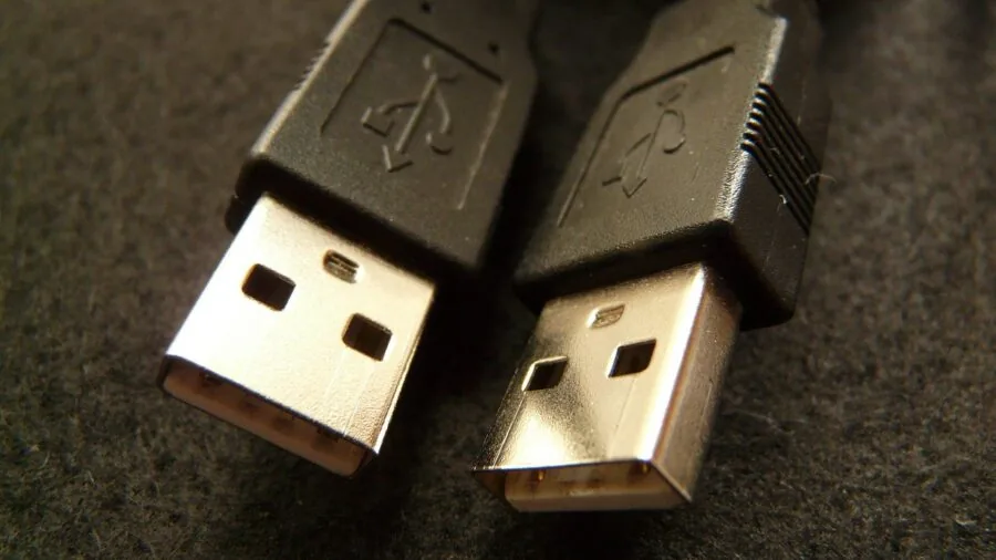 Person plugging USB cable into computer port at desk workspace