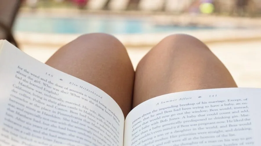 Person reading outdoors by pool in summer, lifestyle scene of leisure and relaxation by water