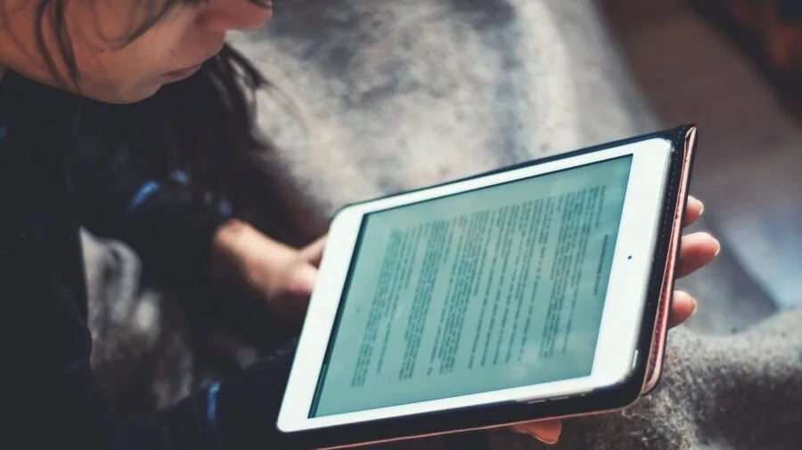 Person relaxing while reading on a digital device, representing e-reader ecosystem choices and content access