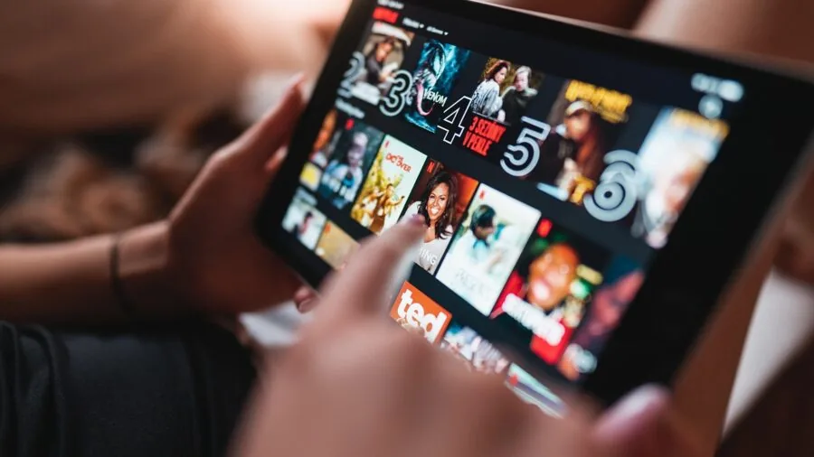Person relaxing while watching a movie on a tablet device in a comfortable home setting