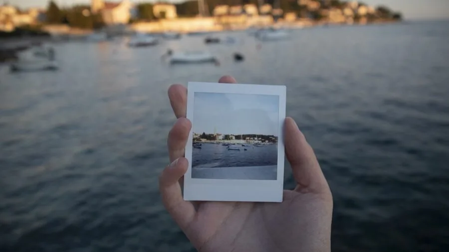 Person reviewing stack of instant film photos, considering cost and value of photography hobby