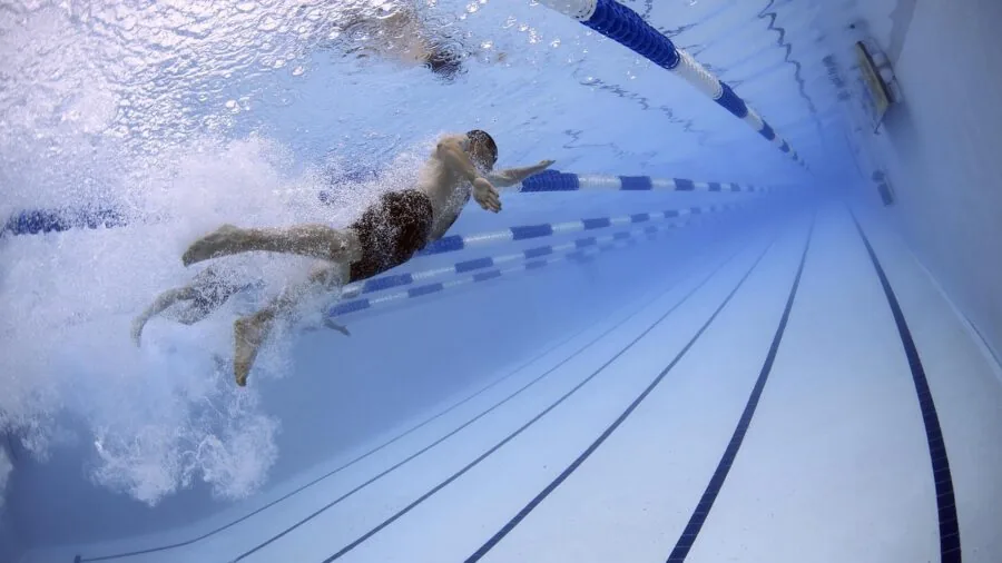 Person swimming freestyle laps in an indoor pool during a fitness workout session
