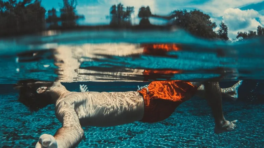 Person swimming underwater with focused expression, experiencing aquatic environment with audio awareness