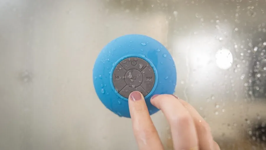 Person testing a waterproof speaker by water in natural outdoor setting