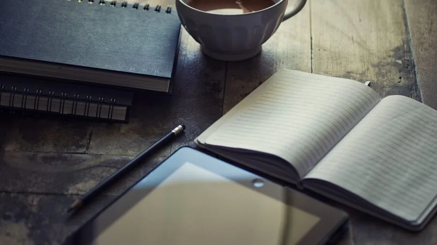 Person using tablet with stylus pen at wooden desk workspace