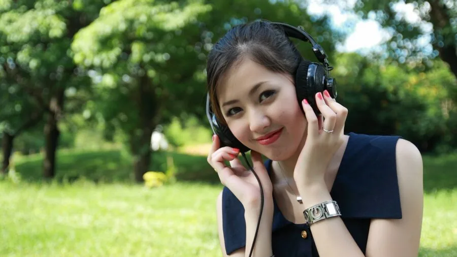 Person wearing glasses outdoors, listening to audio while remaining aware of their surroundings in an open environment.