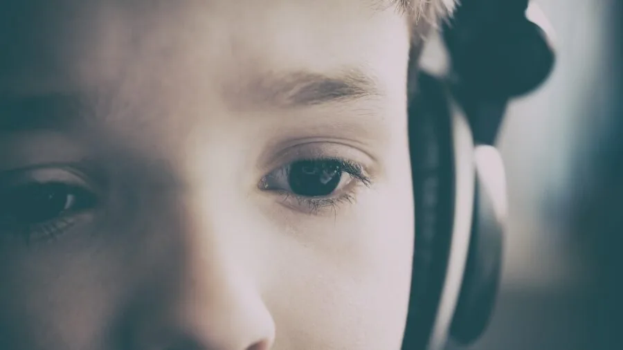 Person wearing headphones at gaming desk with focused expression while adjusting audio equipment settings