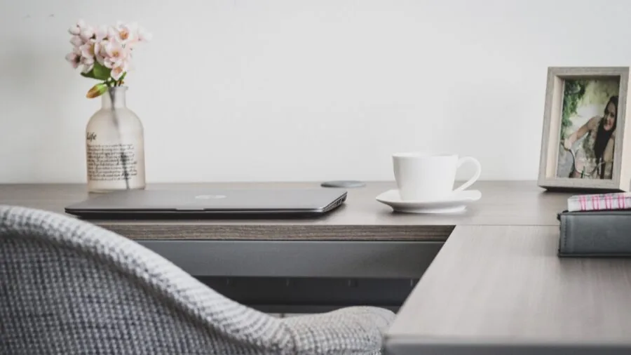 Person working at a clean, organized home office desk with a computer monitor and natural lighting from a window