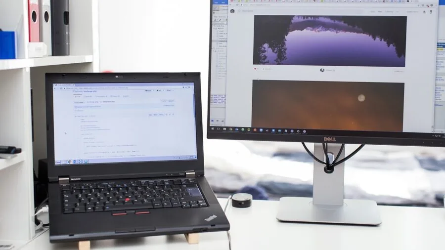 Person working at desk with two monitors connected to laptop in modern home office environment