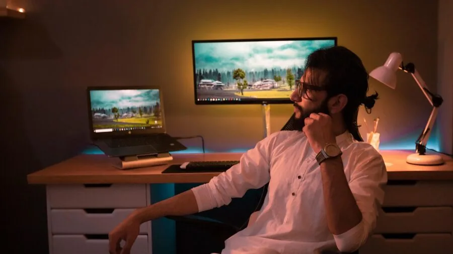 Person working at gaming PC setup with multiple monitors in home office environment for content creation