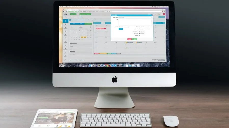 Person working at organized desk with computer monitor, laptop, and gaming controller in modern home office