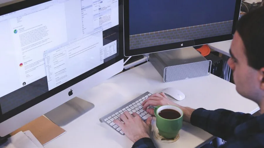 Person working at wooden desk with mechanical keyboard, focused on typing with natural lighting