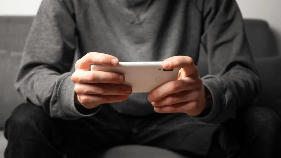 Person's hands holding a smartphone with attached gaming controller in landscape orientation during gameplay