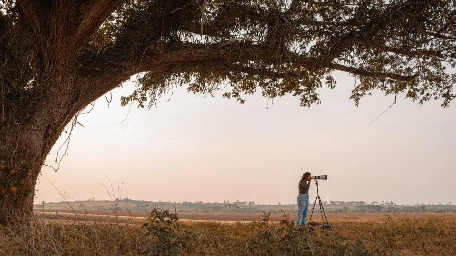 Photographer setting up tripod on rocky terrain during golden hour with wind-blown hair