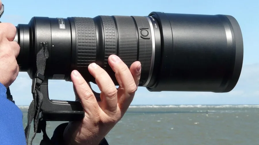 Photographer with telephoto lens capturing distant landscape with steady hands and focused technique