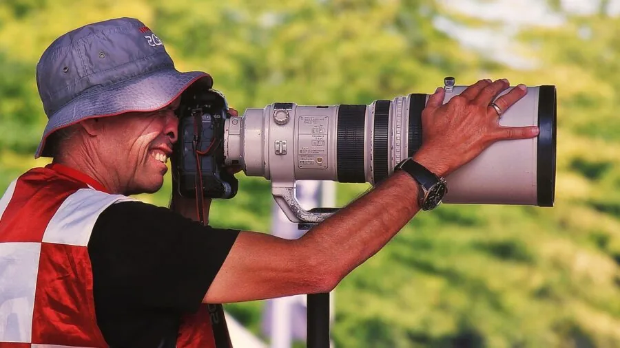 Professional photographer holding telephoto lens steady while capturing distant landscape with careful hand positioning