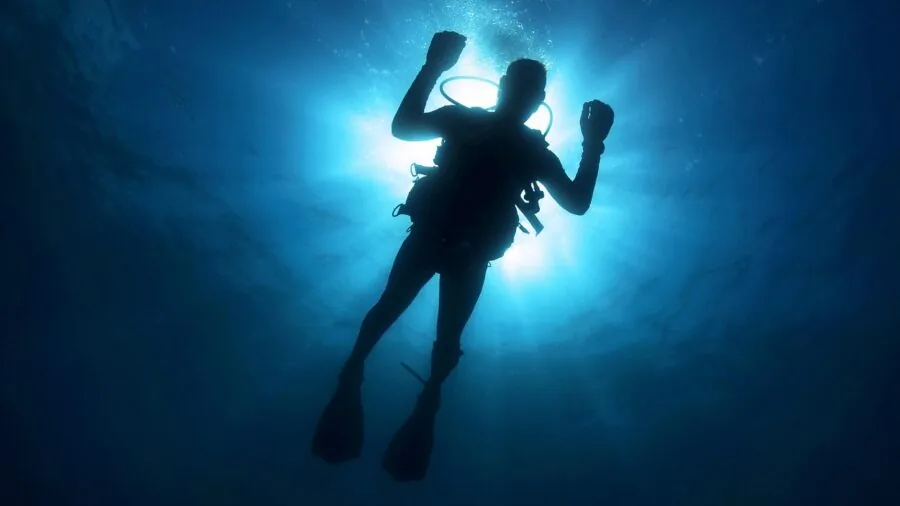 Scuba diver exploring colorful coral reef underwater in clear blue ocean water