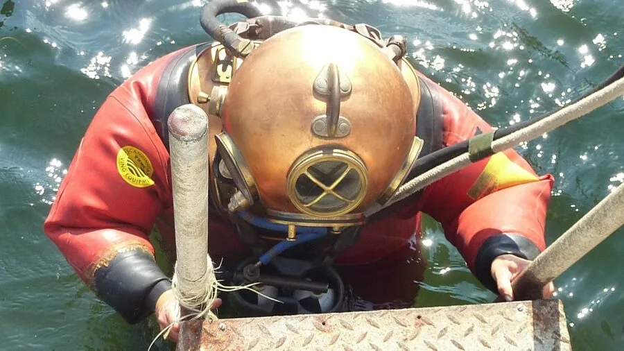 Scuba diver in wetsuit adjusting underwater camera gear while diving in clear blue ocean