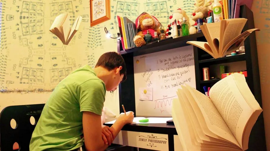 Student focused on computer monitor while studying at desk with notebook and coffee