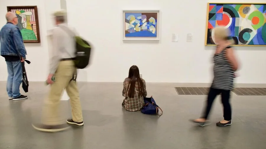 Tourist capturing artwork inside dimly lit museum gallery with camera