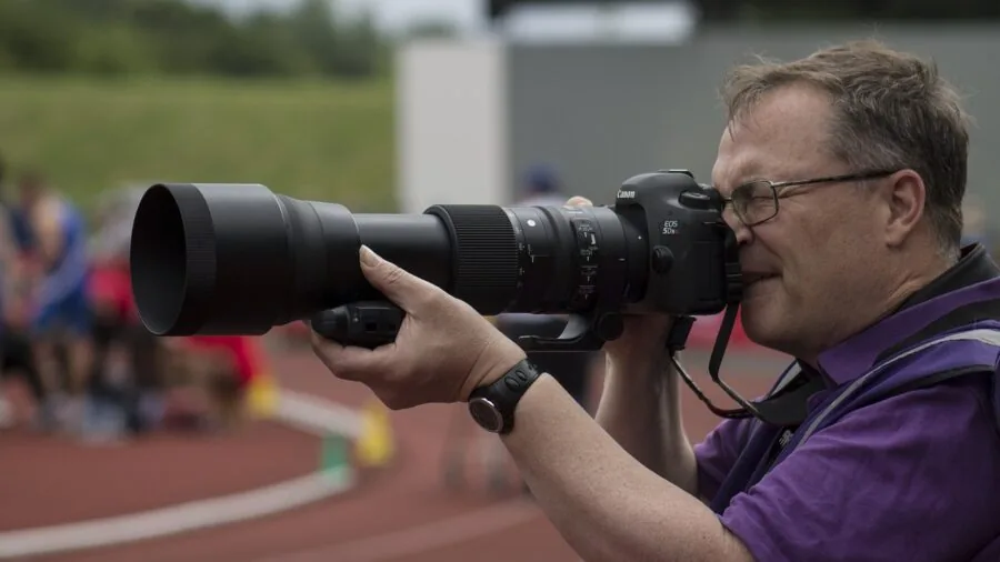 Videographer adjusting camera lens focus while filming outdoor scene