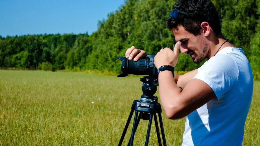 Videographer adjusting tripod head while mounting camera equipment for video production